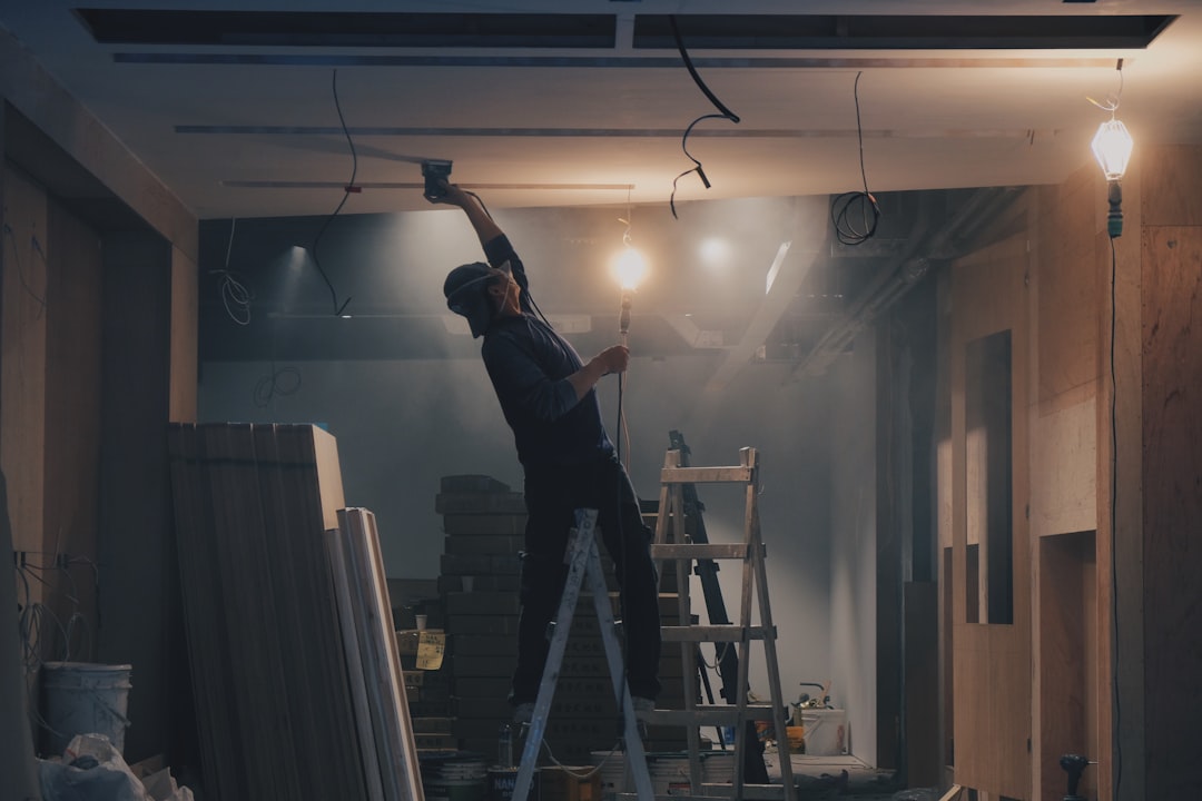 Trabajador empastando y lijando un techo sobre una escalera durante una remodelación
