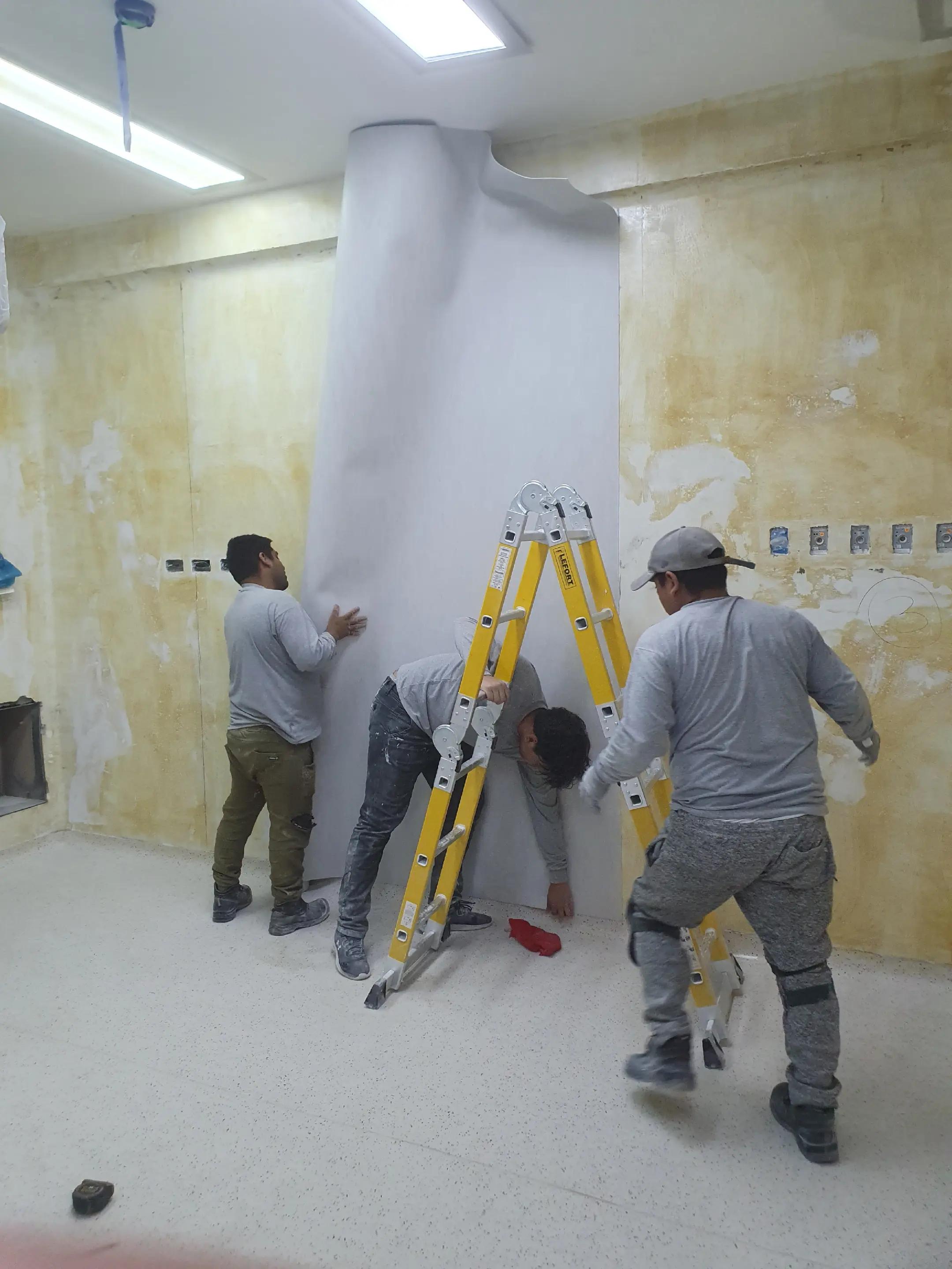 Equipo uniformado de ADN Construcción instalando un panel curvo de pared en la sala DaVinci del Hospital Dos de Mayo, Lima